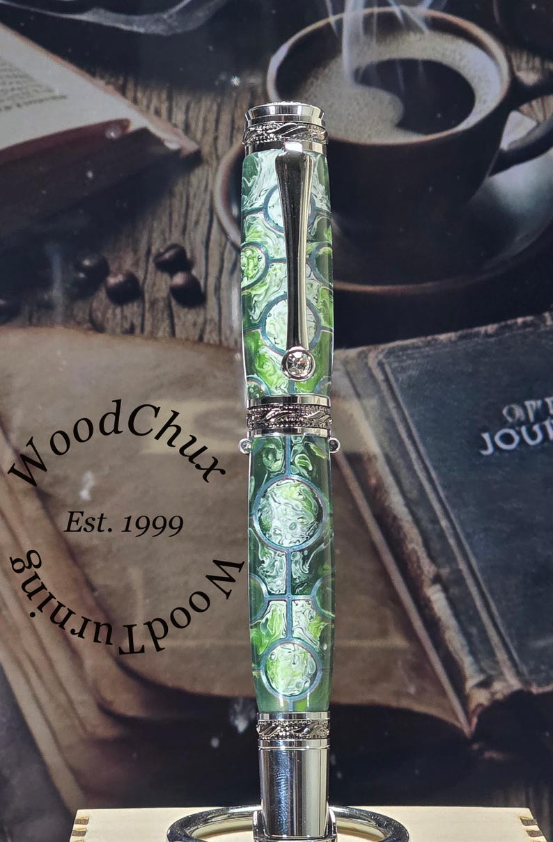 Może przedstawiać: Ręcznie wykonane pi&oacute;ro z zielono-białym wzorem na korpusie, zaakcentowane srebrnymi metalowymi detalami. Pi&oacute;ro posiada ozdobny klips i kryształową ozdobę. Pi&oacute;ro od WoodChux, Est. 1999.