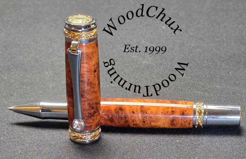 May include: A handcrafted pen with a wooden barrel featuring a unique burl grain pattern. The pen has silver and gold-colored metal accents, including a decorative cap and clip. The pen is lying on a dark surface.