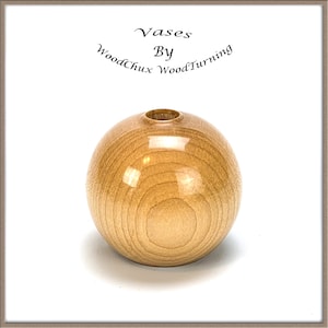 Può includere: Un piccolo vaso rotondo in legno con una finitura liscia e lucida. Il vaso è di colore marrone chiaro e ha una piccola apertura nella parte superiore.