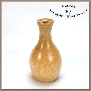 Può includere: Un vaso di legno marrone chiaro con una finitura liscia e lucida. Il vaso ha la forma di una bottiglia tradizionale con una base arrotondata e un collo stretto. È un design semplice ed elegante.