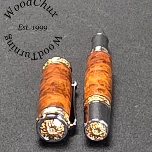 May include: A handcrafted fountain pen with a wooden barrel and a silver-colored clip. The pen's barrel has a unique wood grain pattern with gold accents. The pen cap is detached, revealing the nib. The text "WoodChux" and "Est. 1999" are visible.