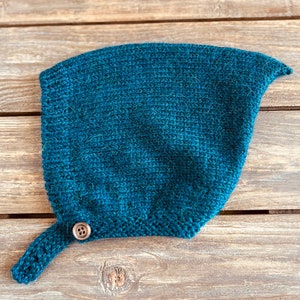May include: A teal blue knitted hat with a pointed tip and a single brown button on the side.