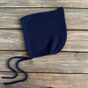 May include: A navy blue knitted baby bonnet with a long tie. The bonnet is made of soft, comfortable material and is perfect for keeping a baby's head warm.