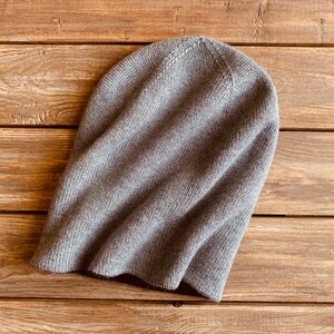 May include: A grey knitted beanie hat on a wooden surface.