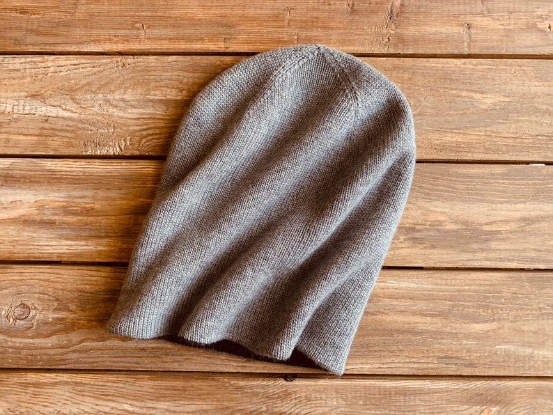 May include: A grey knitted beanie hat on a wooden surface.