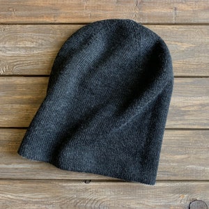 May include: A dark grey knitted beanie hat on a wooden surface.