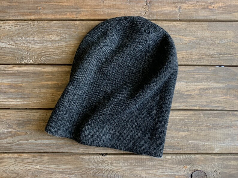 May include: A dark grey knitted beanie hat on a wooden surface.