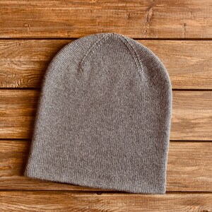 May include: A grey knitted beanie hat on a wooden background.