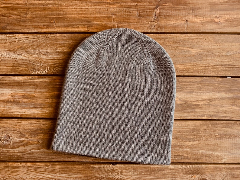 May include: A grey knitted beanie hat on a wooden background.