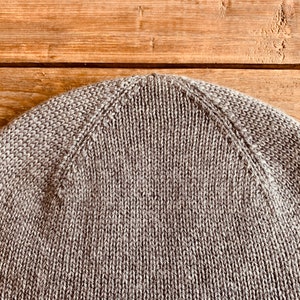 May include: Close-up of the top of a brown knitted beanie hat.