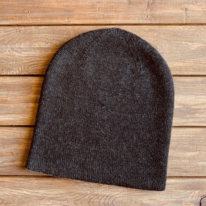 May include: A dark grey beanie hat made of knitted fabric. The hat is on a wooden surface.
