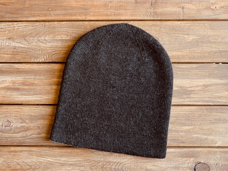 May include: A dark grey beanie hat made of knitted fabric. The hat is on a wooden surface.