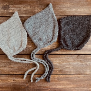 May include: Three knitted baby bonnets in gray, light gray, and black. The bonnets have long ties that can be tied under the chin.
