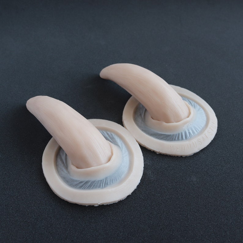 Pair of Oni horns silicone prosthetics in vanilla shade on a black surface at an angle