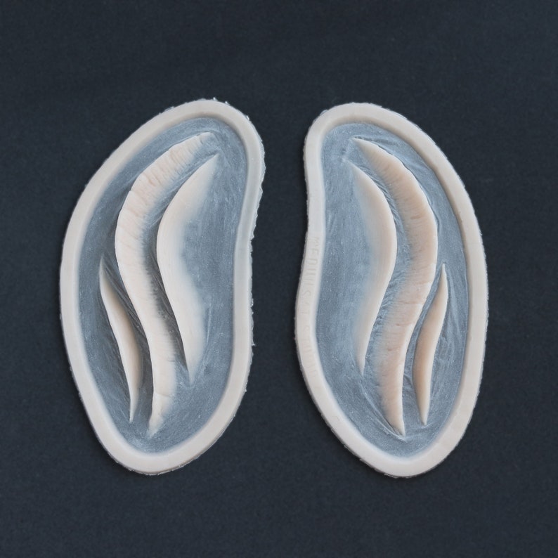 Pair of Mermaid Gills silicone prosthetics in vanilla shade on a black surface