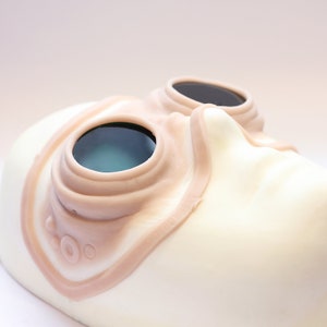 Steampunk silicone prosthetics googles in vanilla shade with green lenses on a white surface