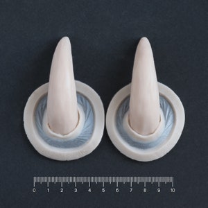 Pair of Oni horns silicone prosthetics in vanilla shade on a black surface with a ruler