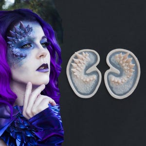 May include: Two silicone moulds for creating prosthetic appliances, each featuring a curved, kidney-shaped design with a textured surface of raised, pointed spikes and scales. The moulds are light beige in colour with a smooth, raised border edge.