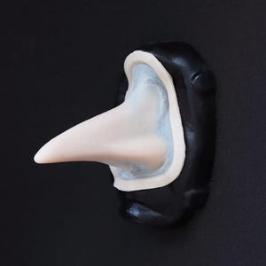 May include: A black and white plague doctor mask with a long, curved beak. The mask has a white beak, a light blue interior, and a black exterior. The mask is made of a smooth material and is set against a black background.
