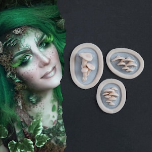May include: Three oval mushroom decorations on a dark background. Each features a different arrangement of small, beige mushrooms set against a light blue backdrop within a cream frame. The image also shows a person with green hair and makeup.