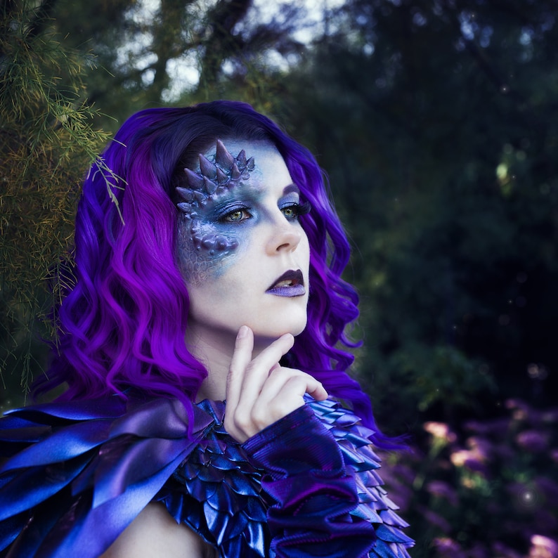 Woman with purple hair wearing a dragon scales prosthetics and purple makeup