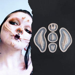 May include: A person with elaborate makeup and facial piercings is shown next to a set of prosthetic pieces. The prosthetics are various shapes and sizes, with a light beige colour and a detailed texture. The background is black.