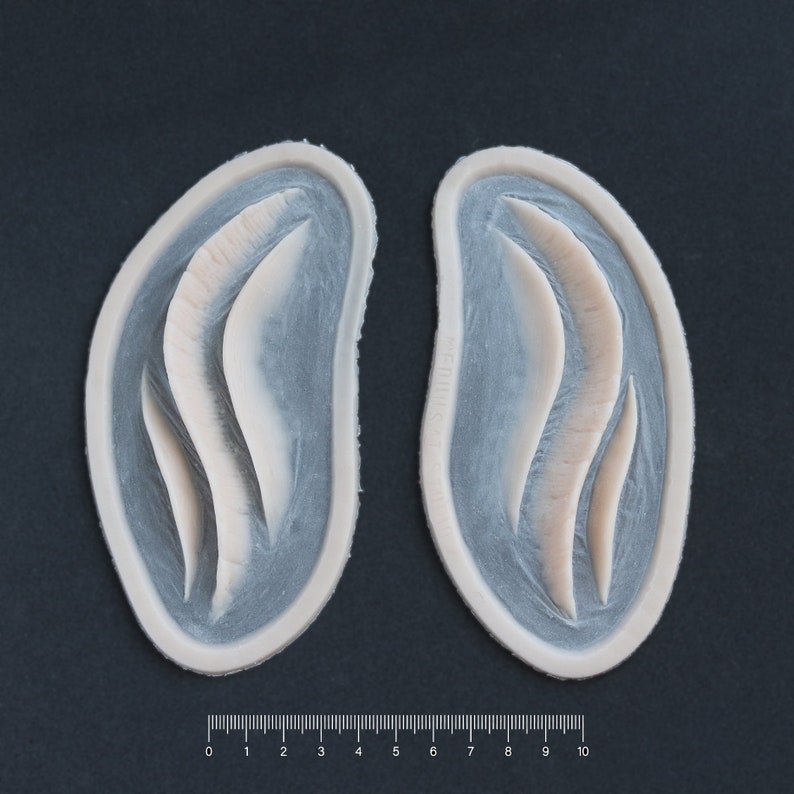 Pair of Mermaid Gills silicone prosthetics in vanilla shade on a black surface with a ruler