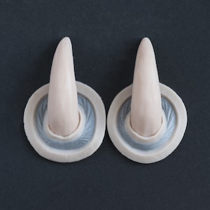 Pair of Oni horns silicone prosthetics in vanilla shade on a black surface