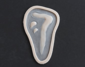 May include: A white ceramic mold shaped like a hand with a raised design of a number seven inside.