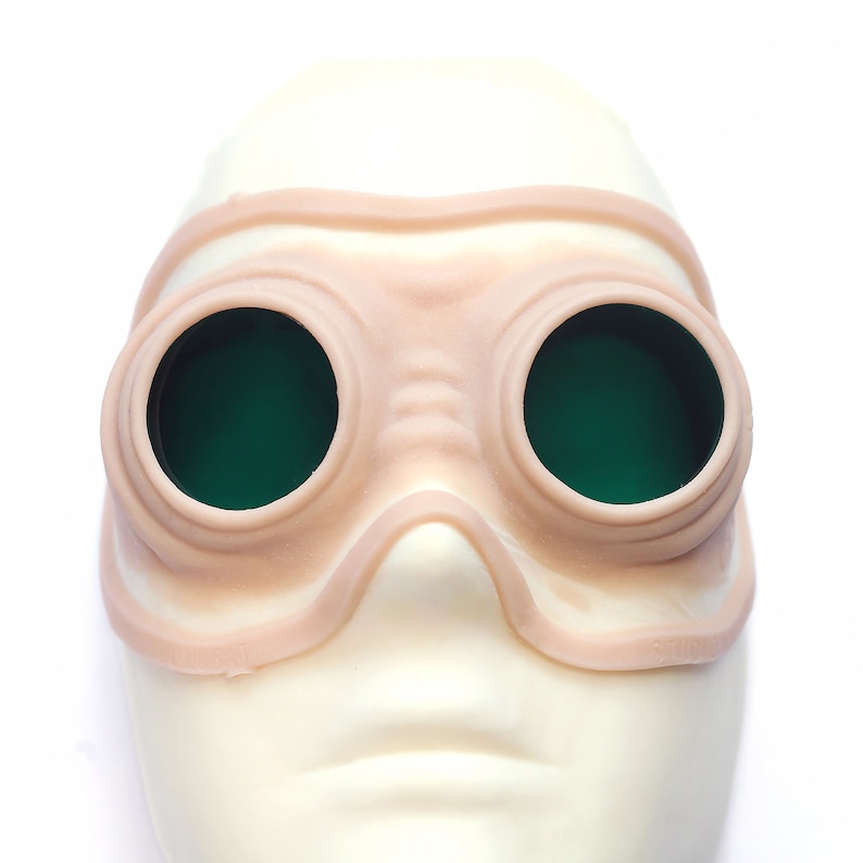 Steampunk silicone prosthetics googles in vanilla shade with green lenses on a white surface