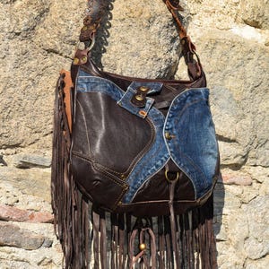 Pu&ograve; includere: Una borsa a tracolla in pelle marrone e denim con dettagli a frange. La borsa ha una tracolla lunga con cuciture decorative e una fibbia in metallo. La borsa &egrave; fatta a mano.