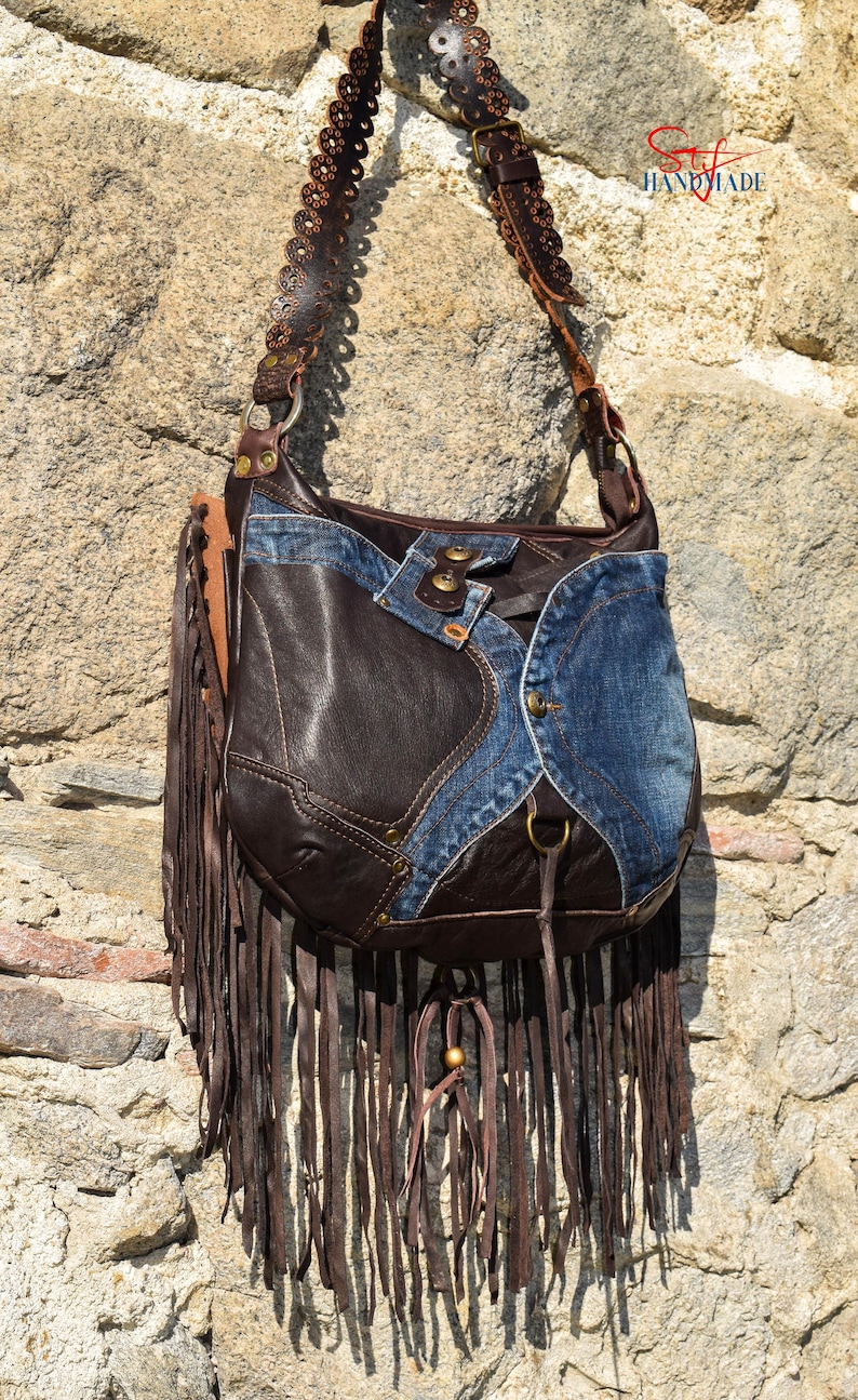 Pu&ograve; includere: Una borsa a tracolla in pelle marrone e denim con dettagli a frange. La borsa ha una tracolla lunga con cuciture decorative e una fibbia in metallo. La borsa &egrave; fatta a mano.