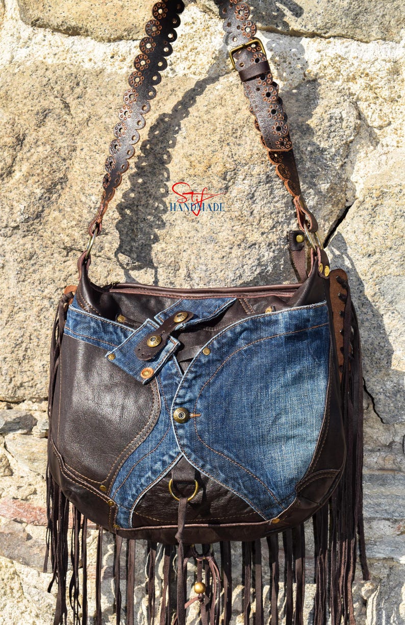 Pu&ograve; includere: Una borsa a mano in pelle marrone con bordi a frangia e un design patchwork in denim. La borsa ha una tracolla lunga e regolabile con tagli decorativi.