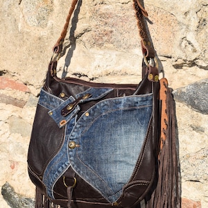 Pu&ograve; includere: Una borsa a tracolla in pelle marrone e denim con dettagli a frange. La borsa ha una tracolla in pelle marrone con cuciture decorative e una fibbia in metallo. La borsa &egrave; fatta a mano.