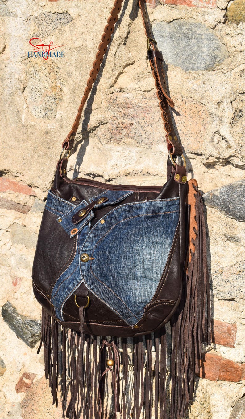 Pu&ograve; includere: Una borsa a tracolla in pelle marrone e denim con dettagli a frange. La borsa ha una tracolla in pelle marrone con cuciture decorative e una fibbia in metallo. La borsa &egrave; fatta a mano.
