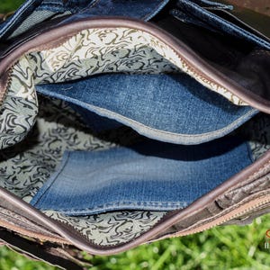 Pu&ograve; includere: L'interno di una borsa in pelle marrone con fodera in denim. La borsa ha una chiusura a zip e una fodera in tessuto fantasia.