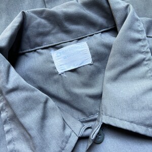 以下が含まれることがあります： 「Big Smith」と「Made in USA」と書かれた白いラベルが付いたグレーの作業着シャツです。