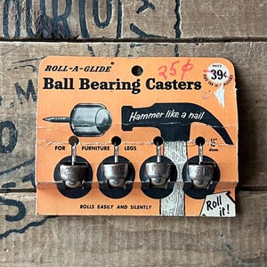 May include: Vintage Roll-A-Glide ball bearing casters on an orange and black cardboard backing. The packaging includes the text "Hammer like a nail" and "Rolls easily and silently". The casters are designed for furniture legs.