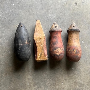 May include: Four antique wooden objects with a weathered appearance. The objects vary in shape, including a teardrop and a truncated pyramid. Colors include black, red, and tan, with visible wood grain and signs of age.