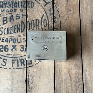 May include: A silver metal bank with a keyhole and the text "JACKSON CITY BANK" and "JACKSON, MICH."