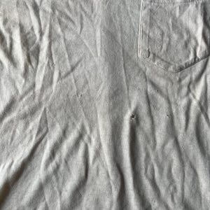 May include: A close-up of a gray, textured fabric with a single pocket. The fabric is wrinkled and has a few small holes.