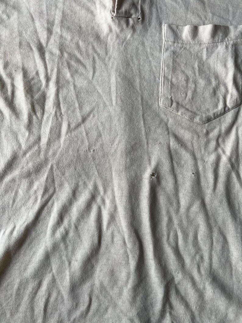 May include: A close-up of a gray, textured fabric with a single pocket. The fabric is wrinkled and has a few small holes.