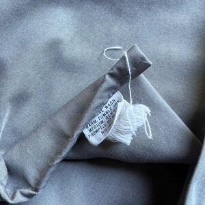 以下が含まれることがあります： グレーの布地のお手入れラベルに、白い文字で「温水で洗濯機洗い。中温でタンブラー乾燥。すぐに取り出す。漂白剤不可。アイロン不可。」と書いてあります