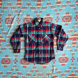 May include: A blue, red, and green plaid flannel shirt with long sleeves and a button-down collar.