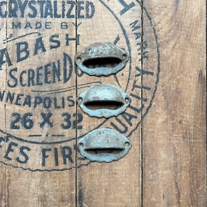 May include: Three antique metal drawer pulls with a light blue finish. The pulls are arranged vertically on a wooden surface with a vintage label that reads "Crystallized Made by Bash Screen Minneapolis 26 x 32" and "Bash" in a circle.