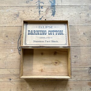 May include: An open wooden box with a label that reads "Eclipse Darning Cotton. Absolutely Stainless Fast Black."