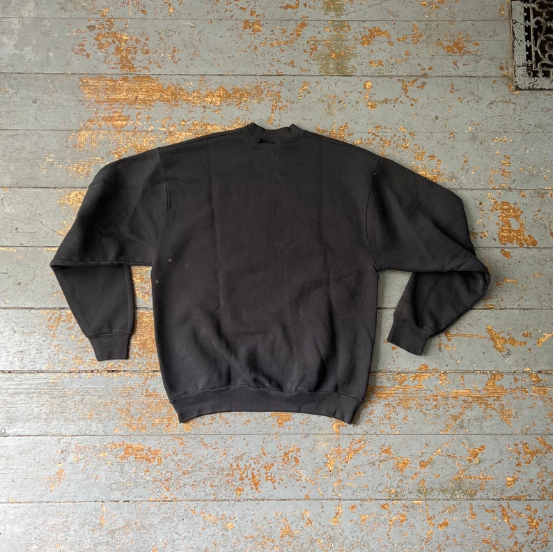 Puede incluir: Sudadera negra de cuello redondo y mangas largas.