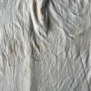 May include: A close-up of a white fabric surface with several brown stains.