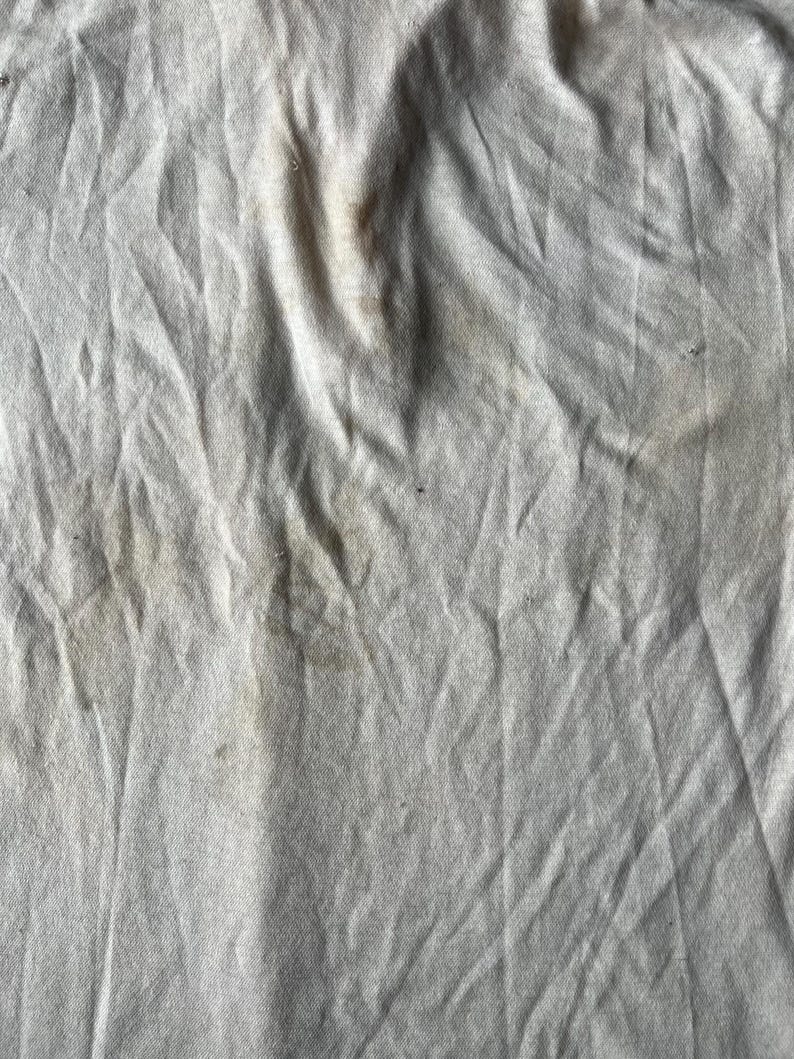 May include: A close-up of a white fabric surface with several brown stains.