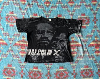 May include: Black t-shirt with a faded image of Malcolm X in black and white. The text "Malcolm X" is printed in white on the front of the shirt.